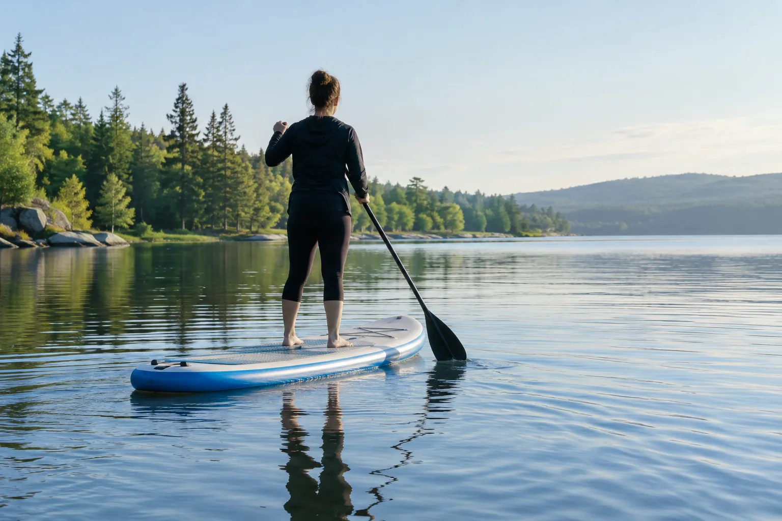 Une personne debout sur une planche de paddle avance sur un lac calme.