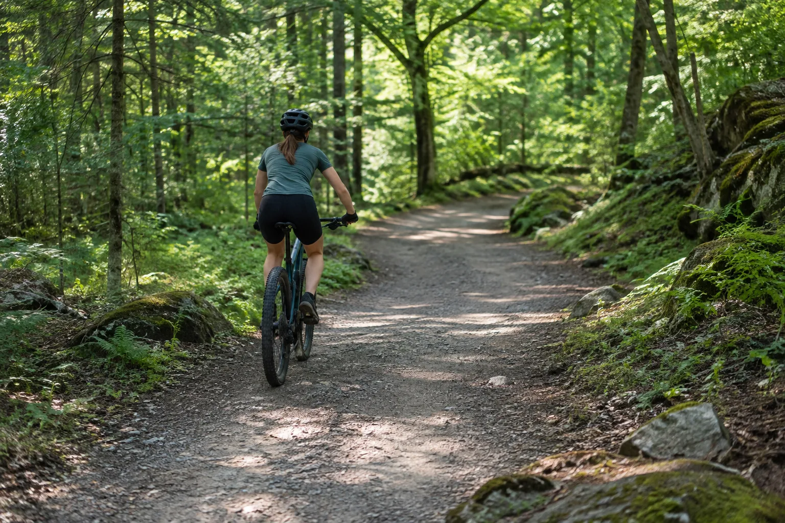 Un cycliste débutant en VTT avance sur un chemin forestier large et facile.